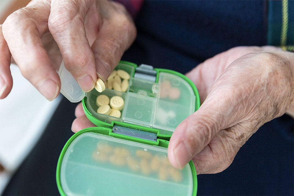 Older adult picks tablet out of pill organizer.