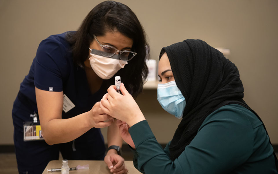 Student pharmacists shown training to prep COVID-19 vaccine to dose patients.