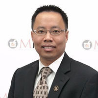 Hoai-An-Truong posed against a light background, wearing a dark suit jacket and tie.