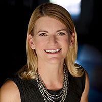 Nicole Brandt posed against a dark background, wearing a silver necklace and smiling.
