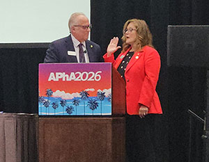 Magaly Rodriguez de Bittner wearing a red jacket, with an APhA sign on stage, being sworn in as president.