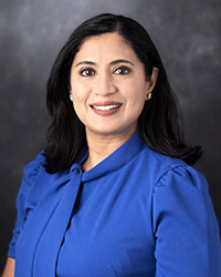 Portrait of Akhila Reddy, wearing a blue blouse, posing against a dark gray background.