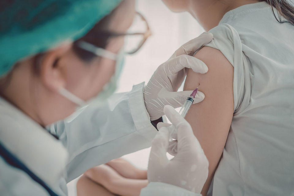 Healthcare worker wearing gloves administers a vaccine injection into a patient’s upper arm.