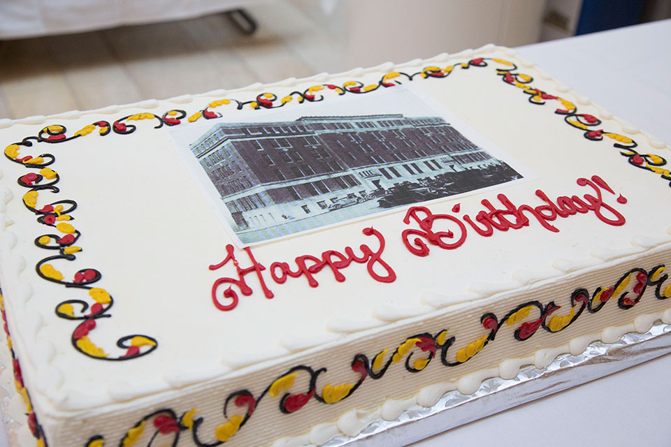 White sheet cake with red and yellow flourishes that says happy birthday with a picture of a black and white building.