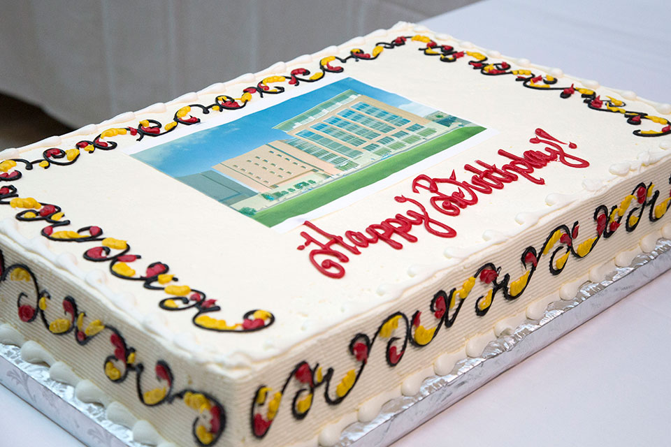 White sheet cake with red and yellow flourishes that says happy birthday with a photo of pharmacy hall.