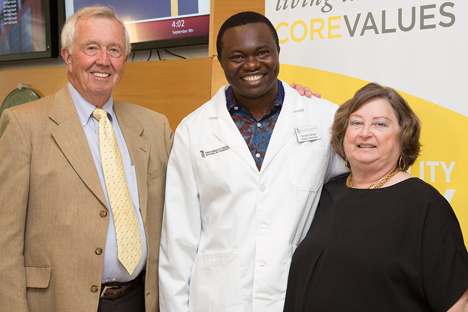 Student pharmacist in white coat posing with two others.