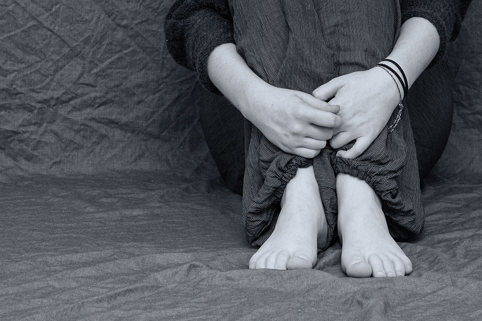Black and white photograph depicts an adolescent with arms wrapped around her knees in distress.