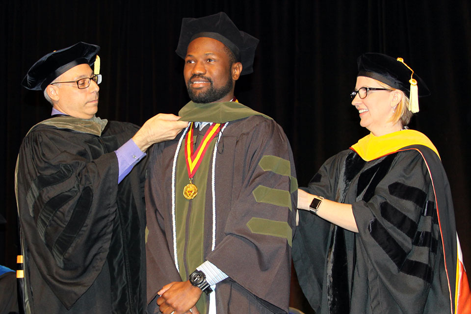 A student receive his PharmD hood from two professors.
