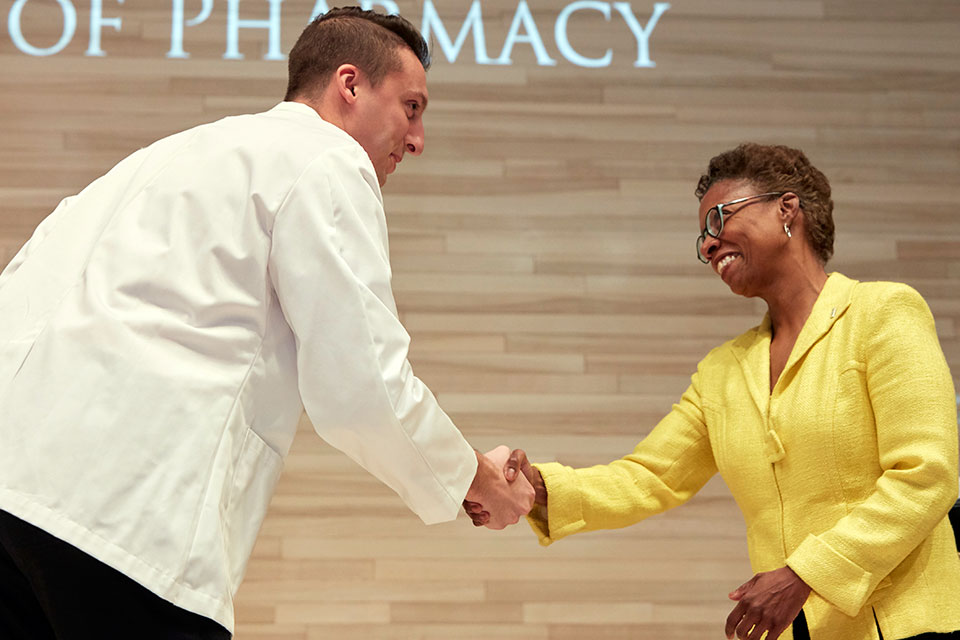 Dean Natalie Eddington shakes hand with student who just received his white coat.