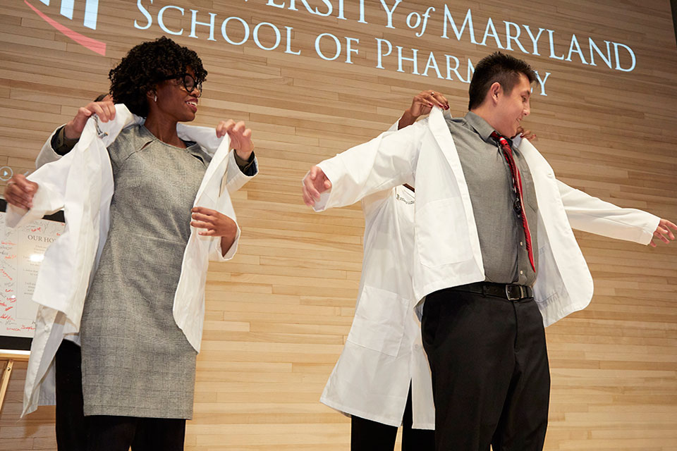 Two first-year student pharmacists receive their white coats from faculty.