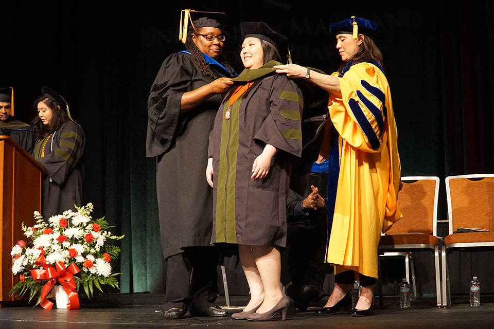 Student pharmacist receives her doctoral hood from Drs. Lisa Jones and Julia Slejko.