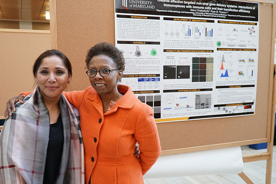 Dean Natalie Eddington poses for photo with postdoctoral fellow presenting research during the symposium's poster session.