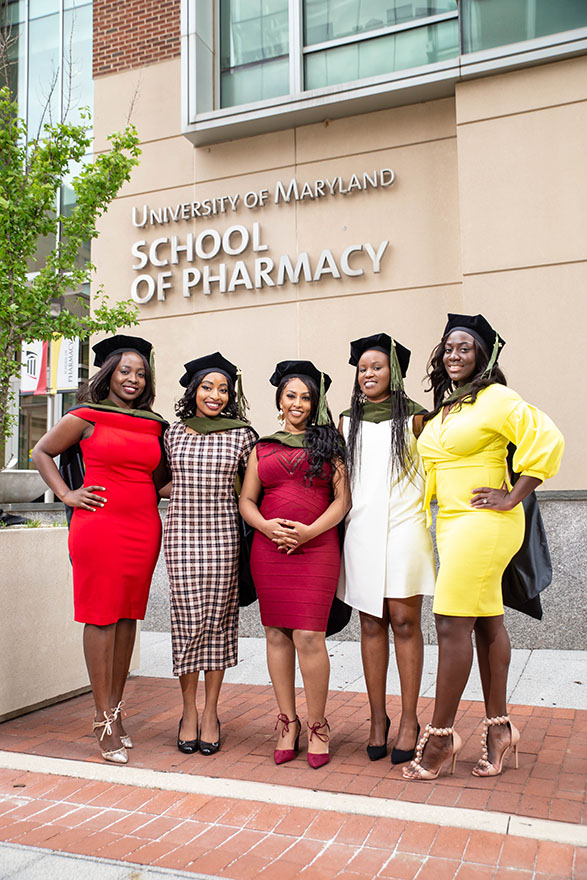 Five student pharmacists pose for photo in graduation regalia outside of Pharmacy Hall.