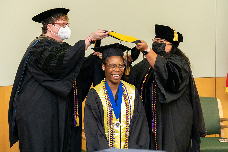 A student ducks while getting hooded at the 2022 palliative care graduation.