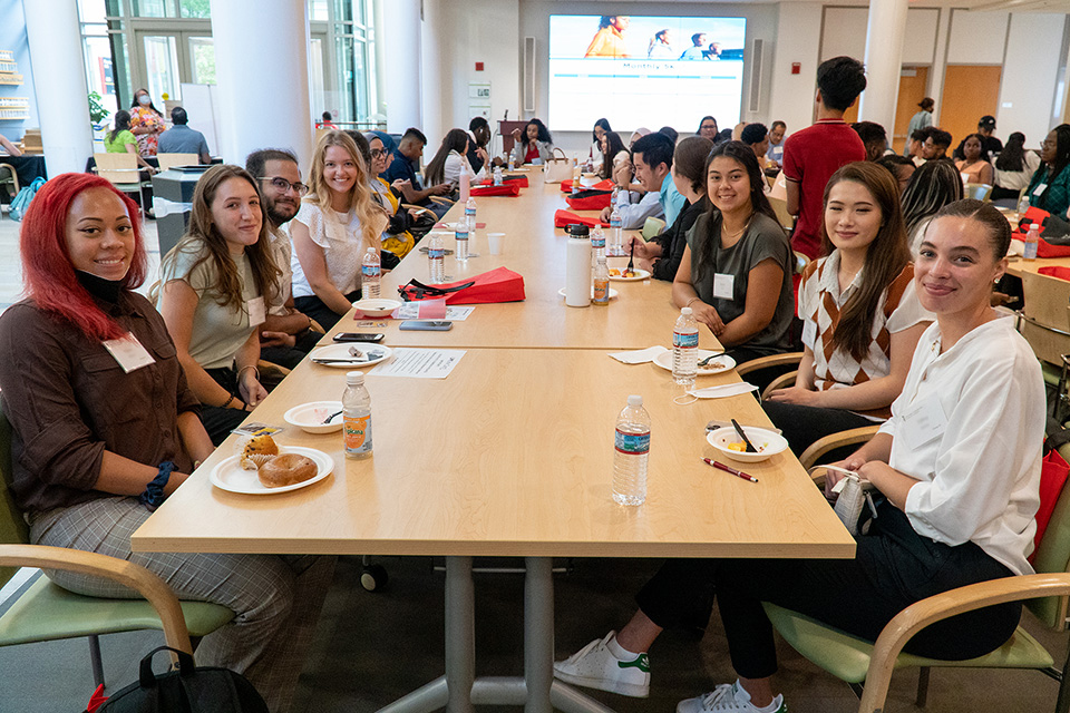 Students sit at a long table in Pharmacy Hall and meet each other.