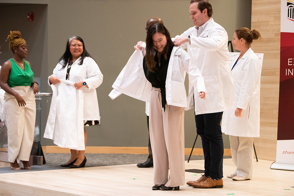 Faculty help students putting on their white coat on stage.