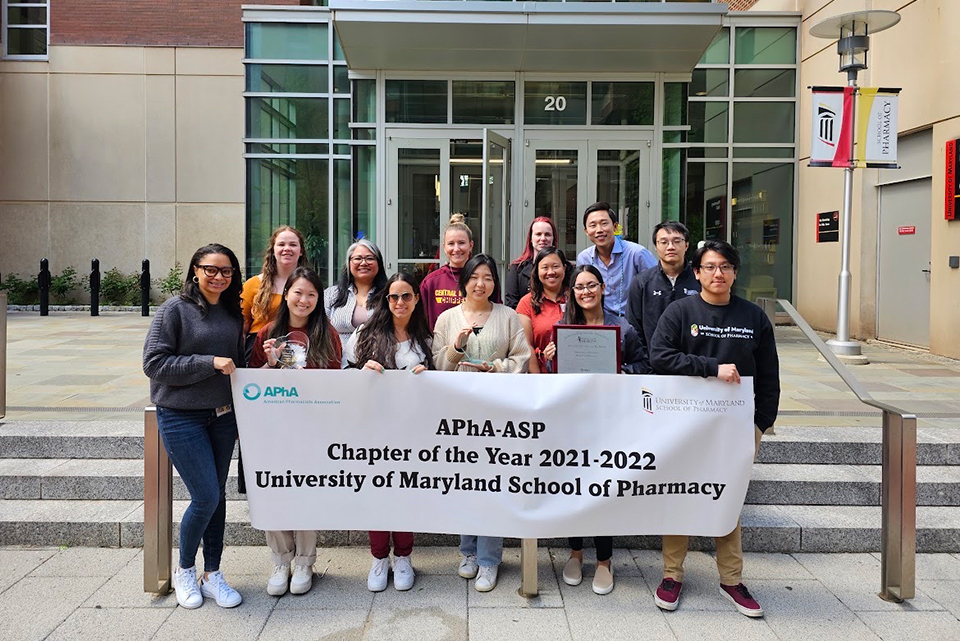 Group photo of the APhA-ASP student chapter outside Pharmacy Hall with a banner celebrating their chapter of the year award for 2021-22.