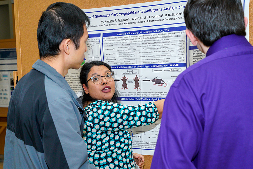 A student explains a poster to two people during the UMB-JHU Drug Discovery Symposium
