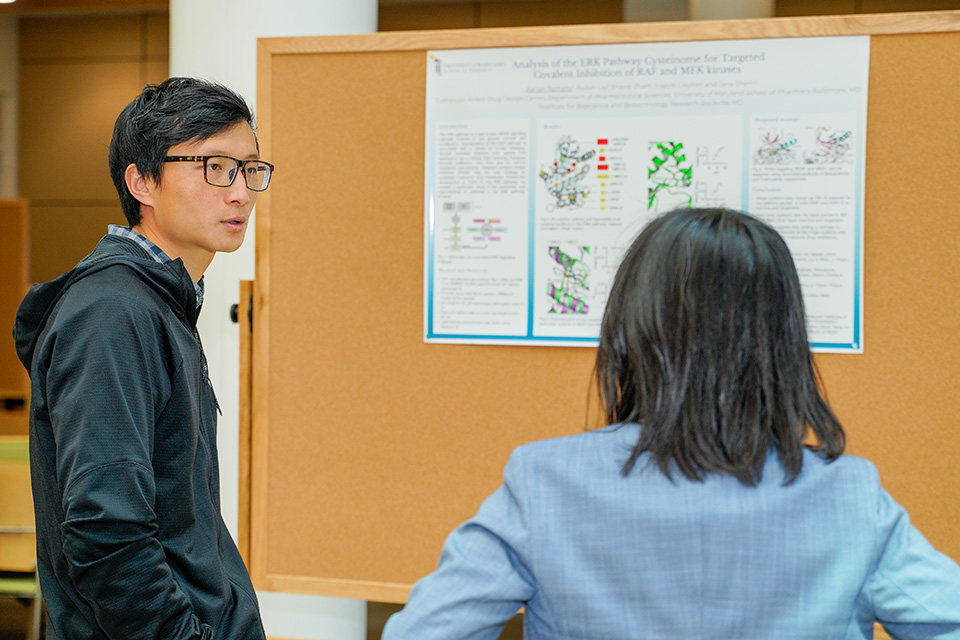 Two people discuss a poster at the CADD symposium.