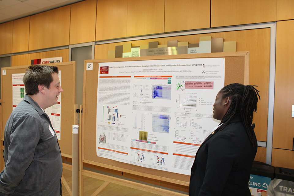 A researcher describes their work to another person at the FCBIS poster session.