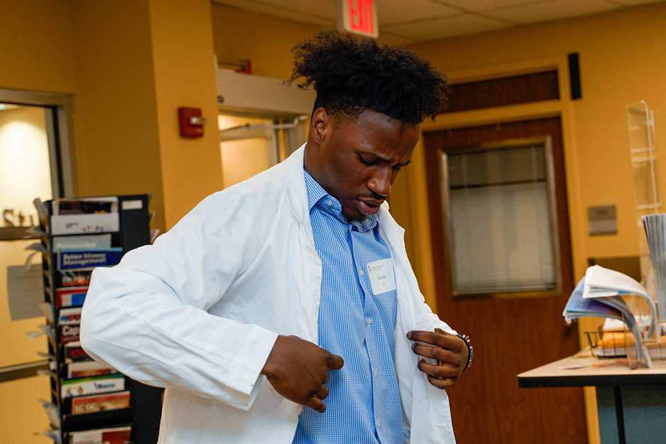 An incoming student tries on a white coat.