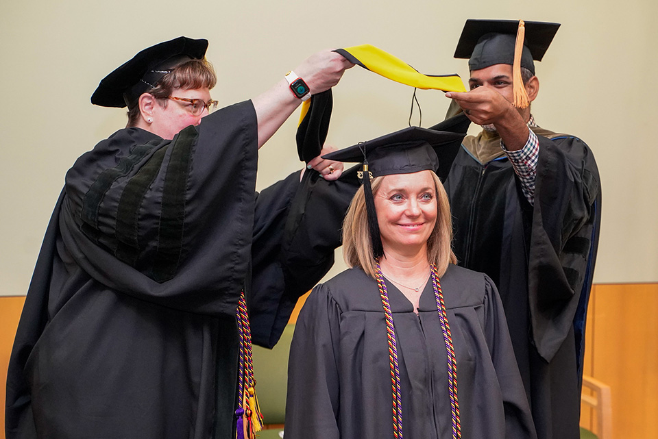 A student prepares to be hooded at the palliative care graduation.