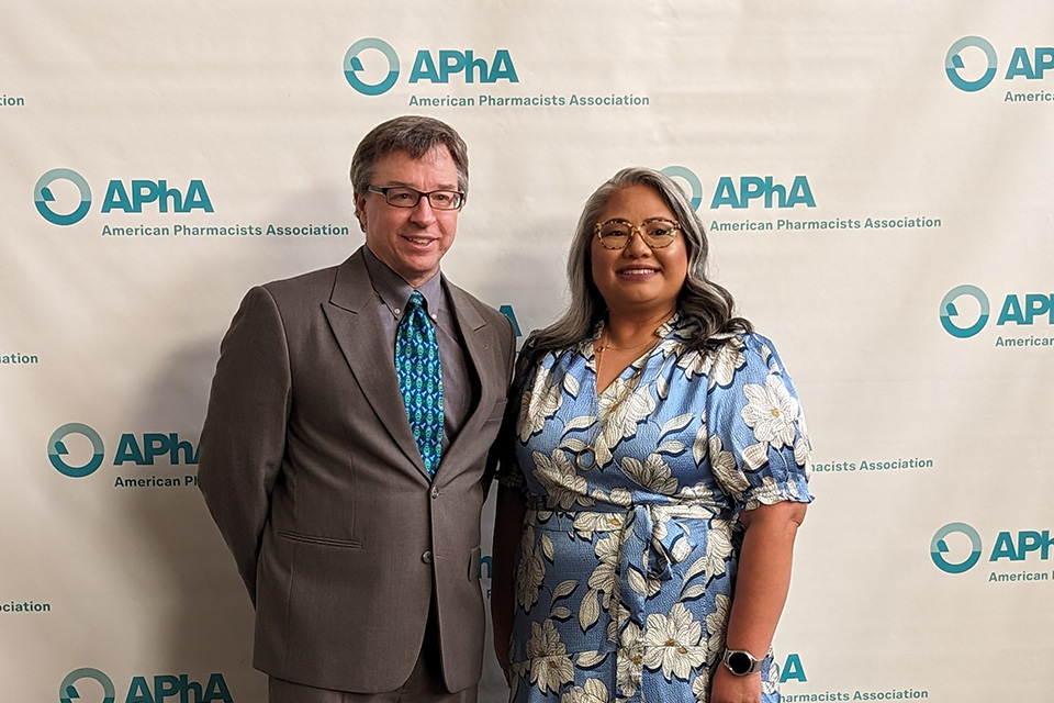 Jim Polli and Cherokee Layson-Wolf posing in front of an APhA backdrop.
