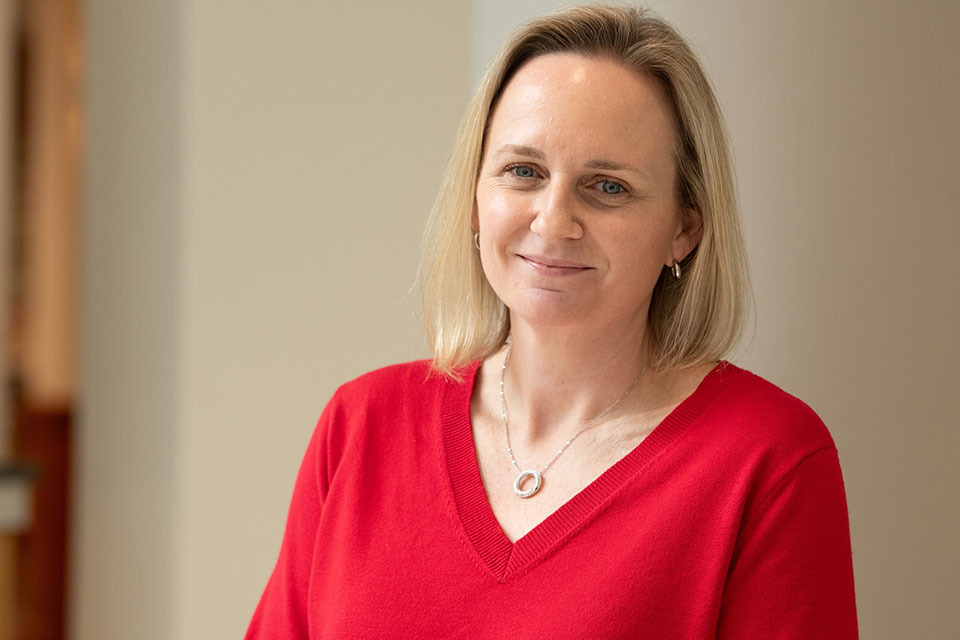 Lisa Finn wearing a red V‑neck sweater and silver necklace, posed indoors against a neutral background