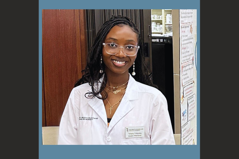Tiffany Frimpong wearing a white lab coat in a pharmacy, standing beside a health information display.