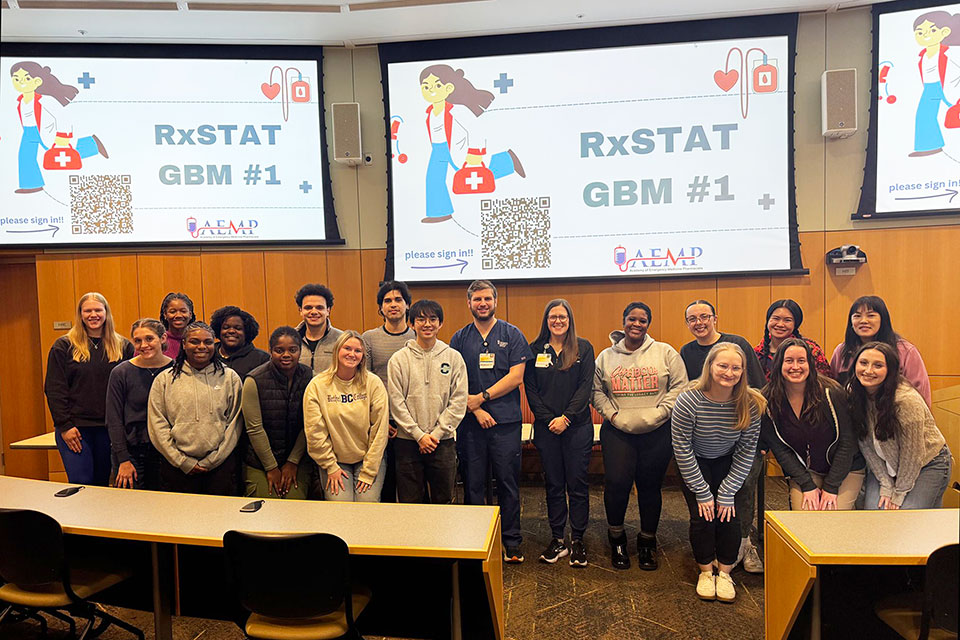 Students standing in a lecture hall in front of screens displaying ‘RxSTAT GBM #1