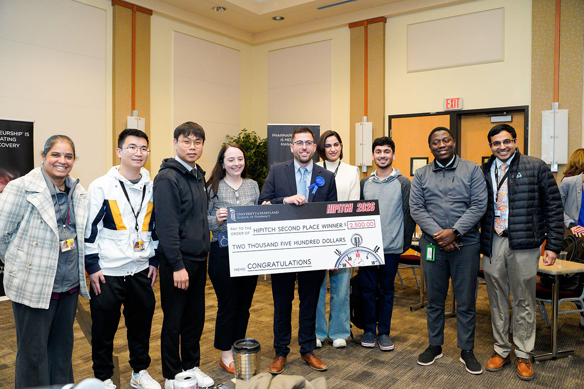Athanasios Chamzas holds a HiPitch second‑place check while posing with members of the University of Maryland School of Pharmacy community at the HiPitch finals.