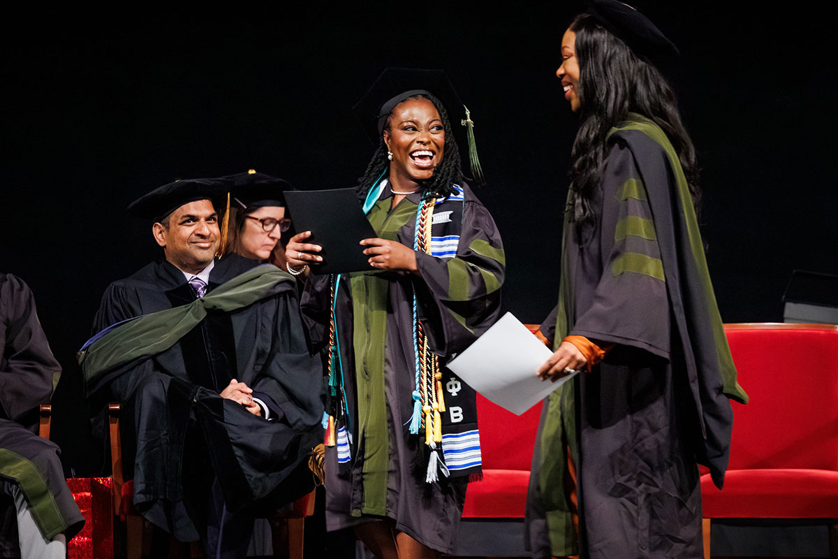 Sandeep Devabhakthuni sits at left on stage as a graduate receives recognition during the PharmD graduation ceremony.