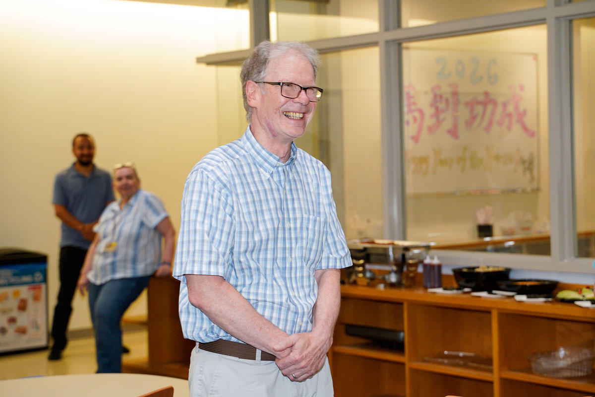 Richard Dalby standing indoors smiling with two colleagues in the background.